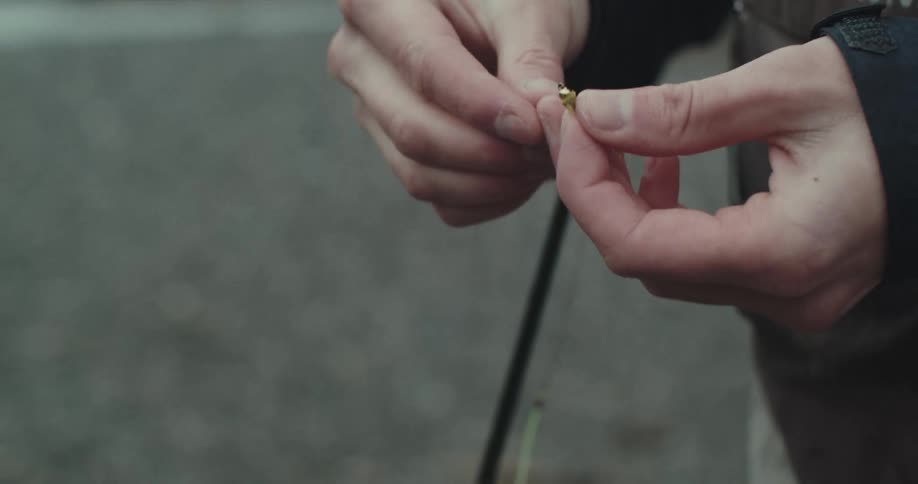 Persons arm setting a fishing hook into a fishing line beside a stream at midday