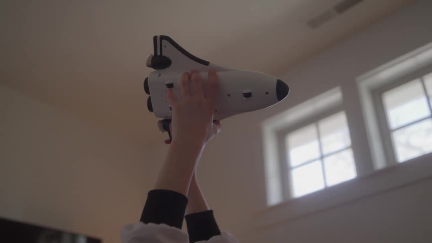 Kid playing indoors with a toy airplane hovering it in circles through the air