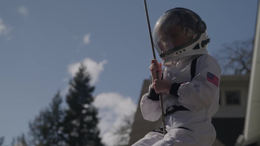 Little girl dressed as an astronaut playing on a swing