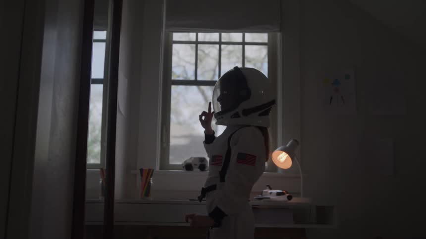 Girl dressed as an astronaut putting on her helmet in front of the mirror in her bedroom