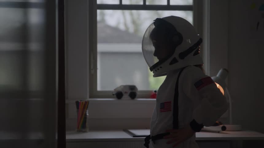 A girl wears a space suit and puts on a helmet while standing in a room
