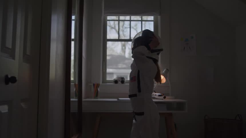 Girl dressed as an astronaut putting on a helmet inside the room