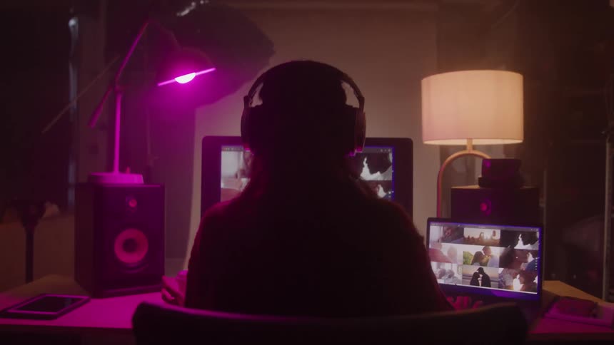 Silhouette of a woman putting on headphones and working in front of a computer in a dimly lit room