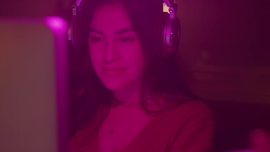 Woman with headphones in a room with pink lighting in front of the computer