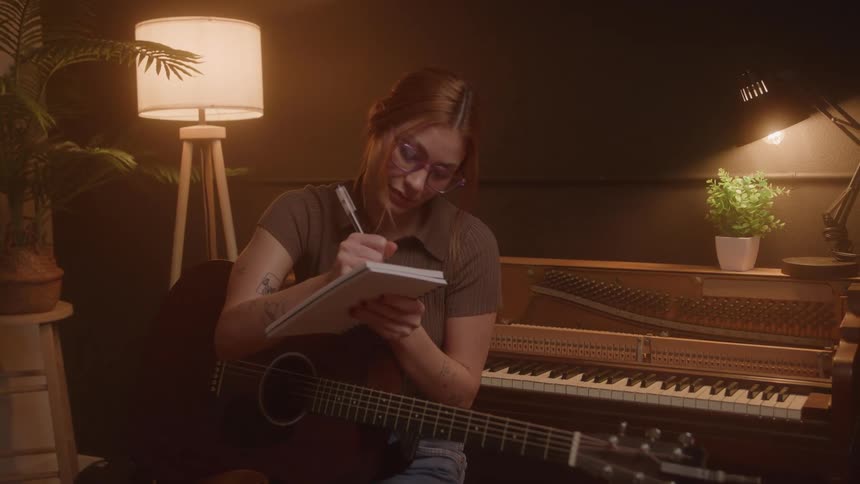 Woman sitting with a guitar taking notes in a notebook