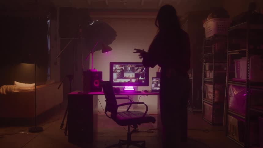 Young woman standing from a chair in front of a computer answering a phone call while scrolling on her pc with a mouse