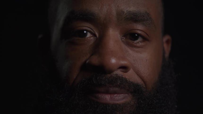 A man with a beard and a serious look turns his head to his side and stares