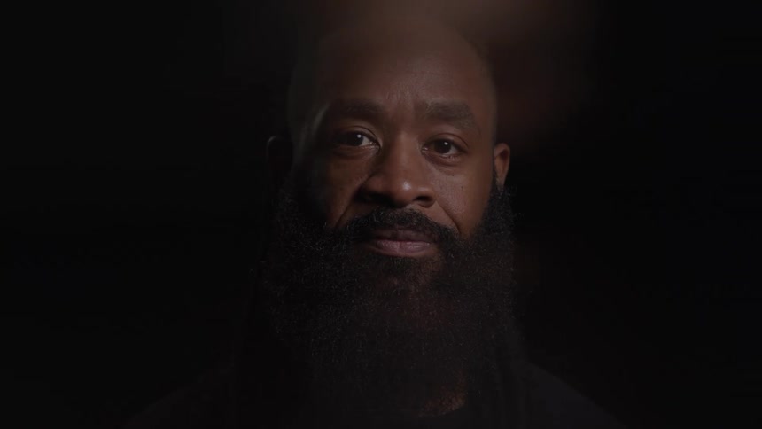 A mans face and shoulders as he turns his head to look at the camera and smiles