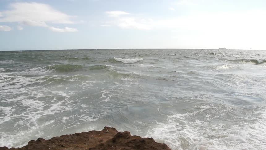View off a stone cliff onto a wavy shore