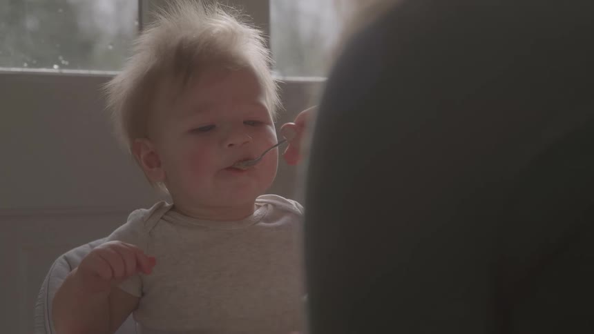 Adult person feeding a blond baby with a spoon