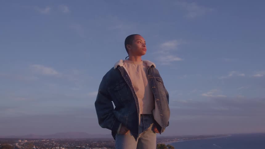 The woman is standing on a mountain looking up at the sky