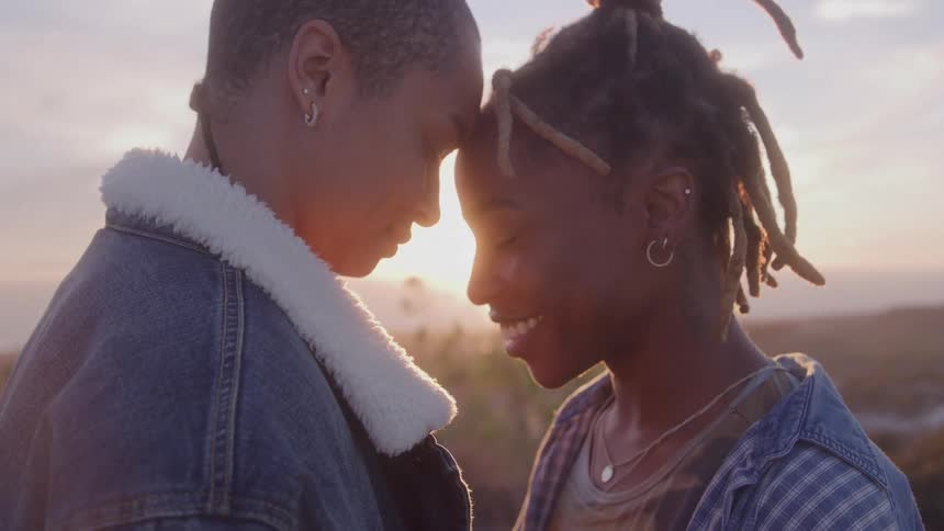 An affectionate couple gently touches foreheads as the sun sets beautifully between them creating a lens flare