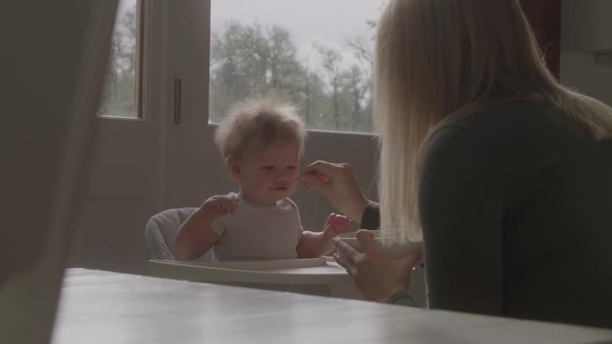 The mother reaches with a spoon to feed her baby