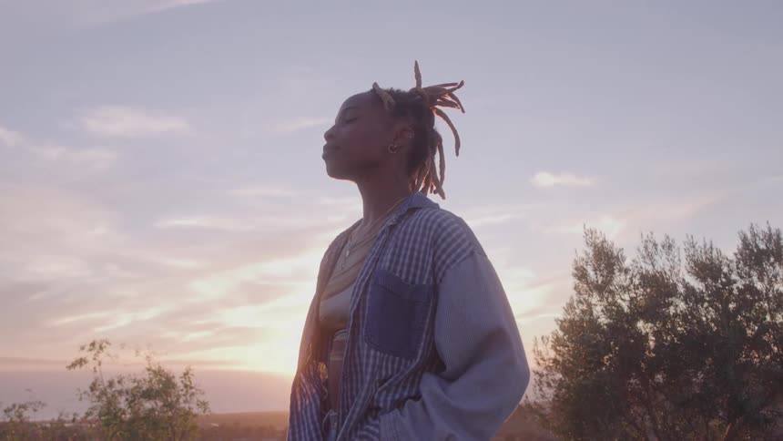 The woman is looking up at the sky at sunrise