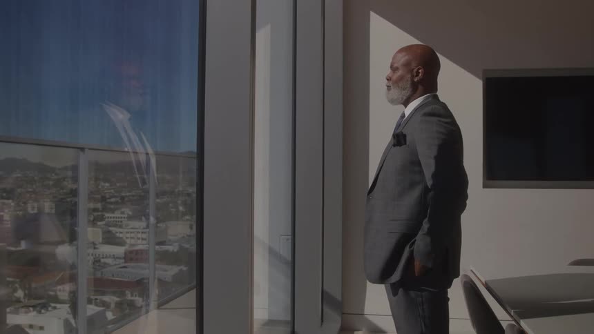 The man stands by the conference table looking out the window