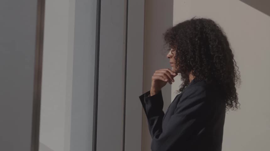 A woman in business clothes stands looking out a window