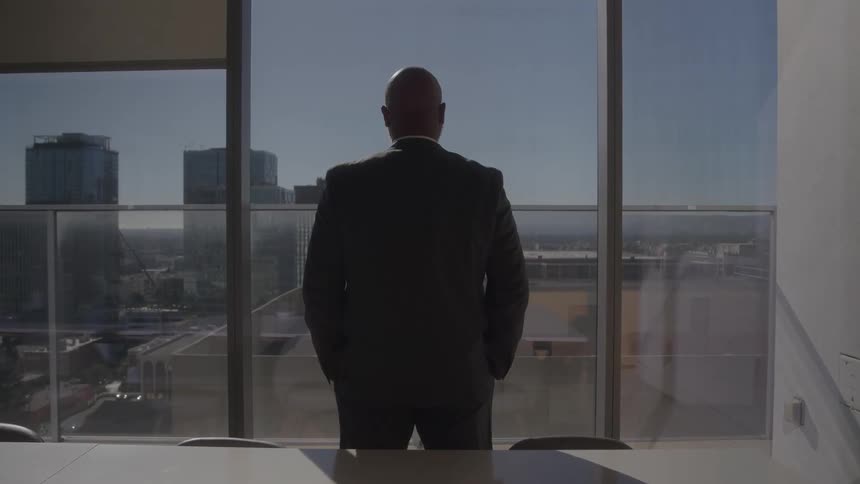 Man in suit looking out of panoramic window overlooking a city