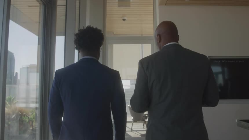 Two men in business suits walk and talk in a building hallway