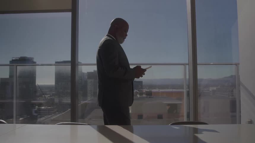 Middleaged black man with a bald head using his mobile device at midday in a highrise conference room