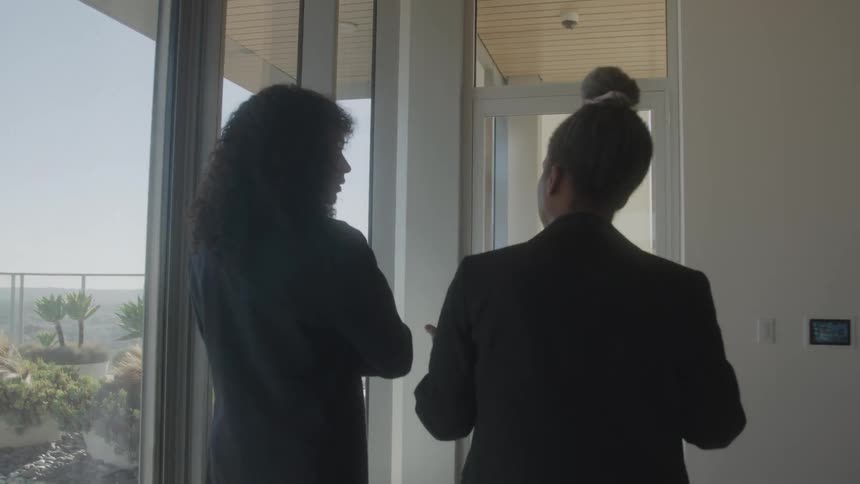 Two women in suits talking as they walk side by side on a hallway leading to an office