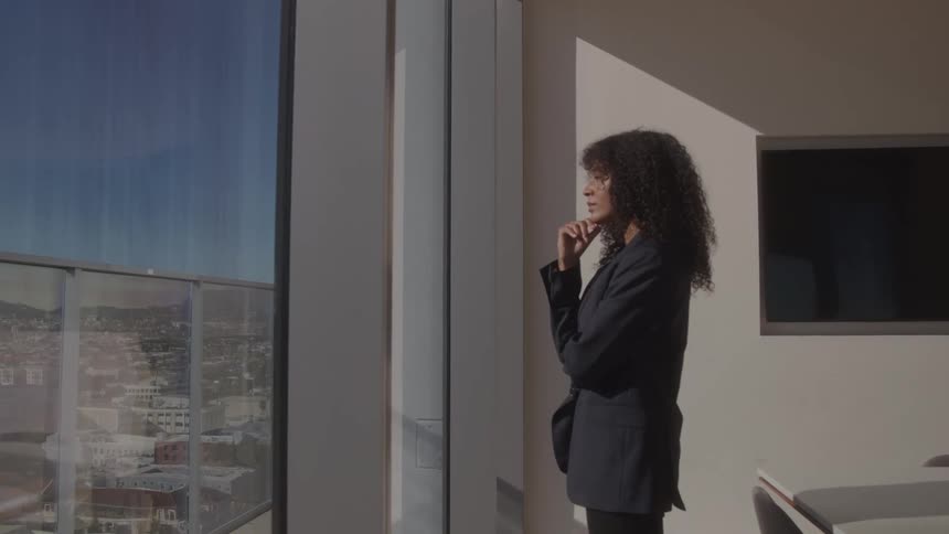 The woman views the city from the office window during the day