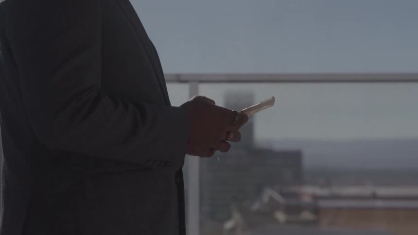 The man texts on his phone in front of the large window