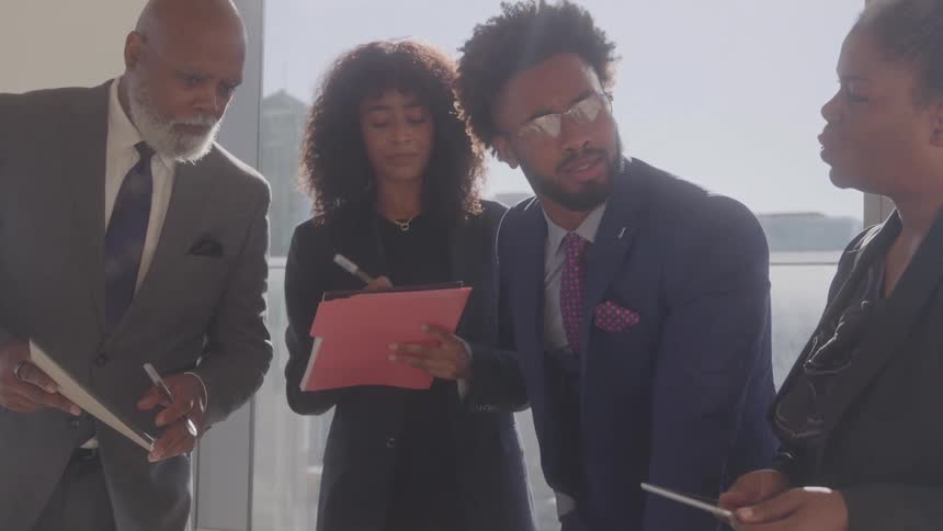 A group of four black executives discussing while standing in an office during daytime