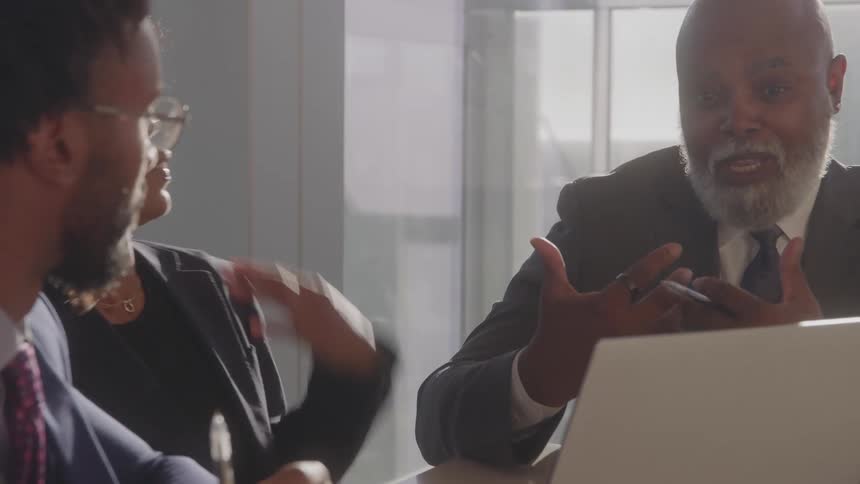 Two men and a woman in formal wear talk in an office meeting