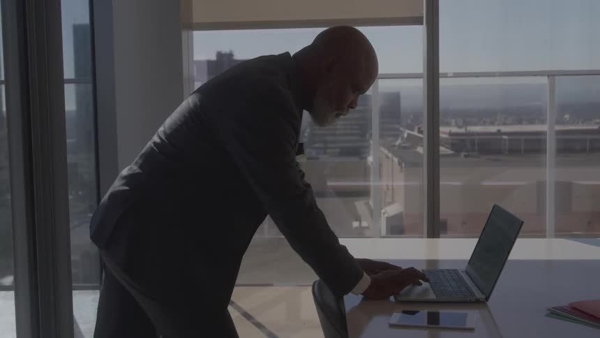 Man in a suit in an office room facing a laptop on the table