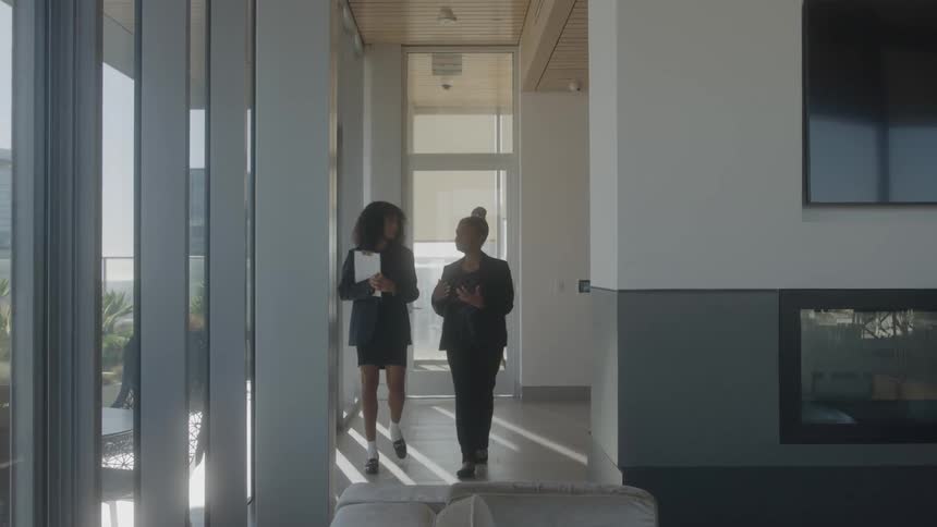 Two women walk down an office hallway and talk