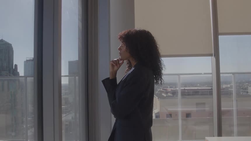 The woman is thinking about something as she looks out the large window