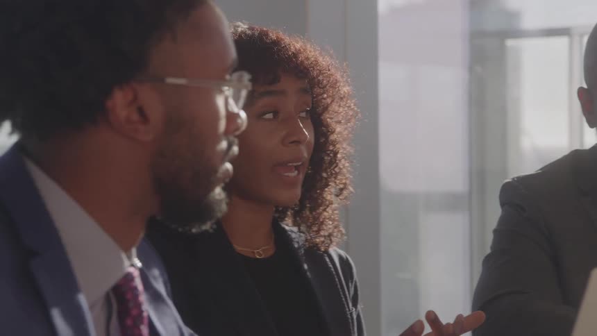 Three people in an office sit and talk around a table