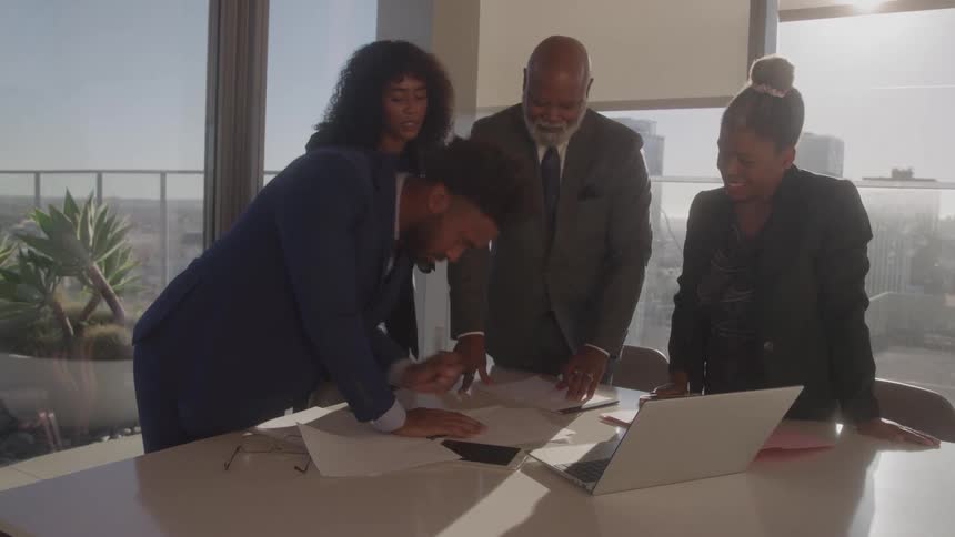 Four people signing a document at an office desk
