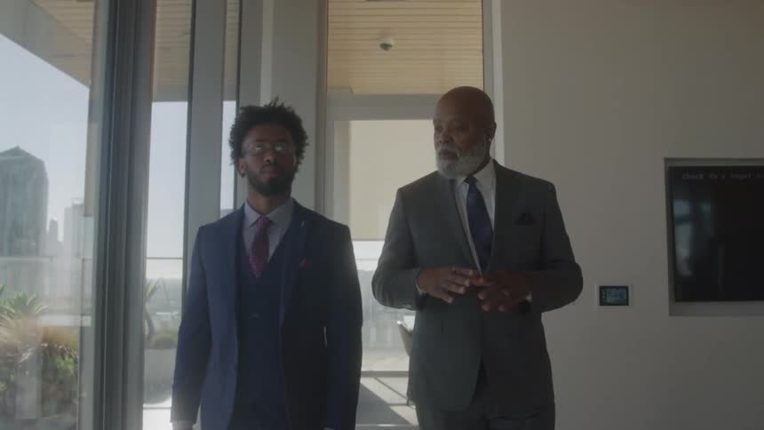 Two black male executives discussing while walking together in an office during daytime
