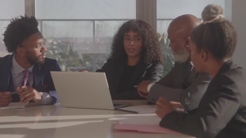 A group of four black executives discussing at a table in an office during daytime