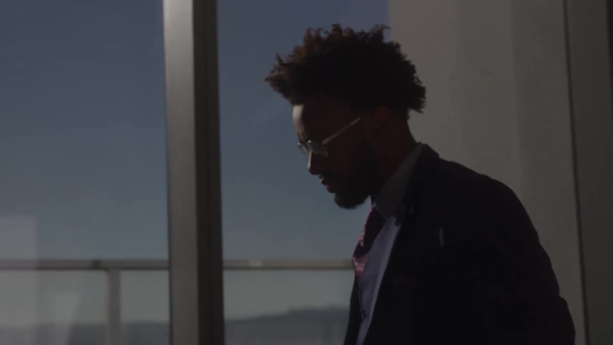 Close up of a young black male executive pacing around an office during daytime