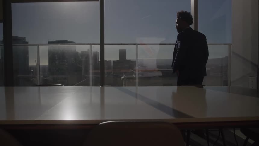 A young black male employee pacing around in a conference room during daytime