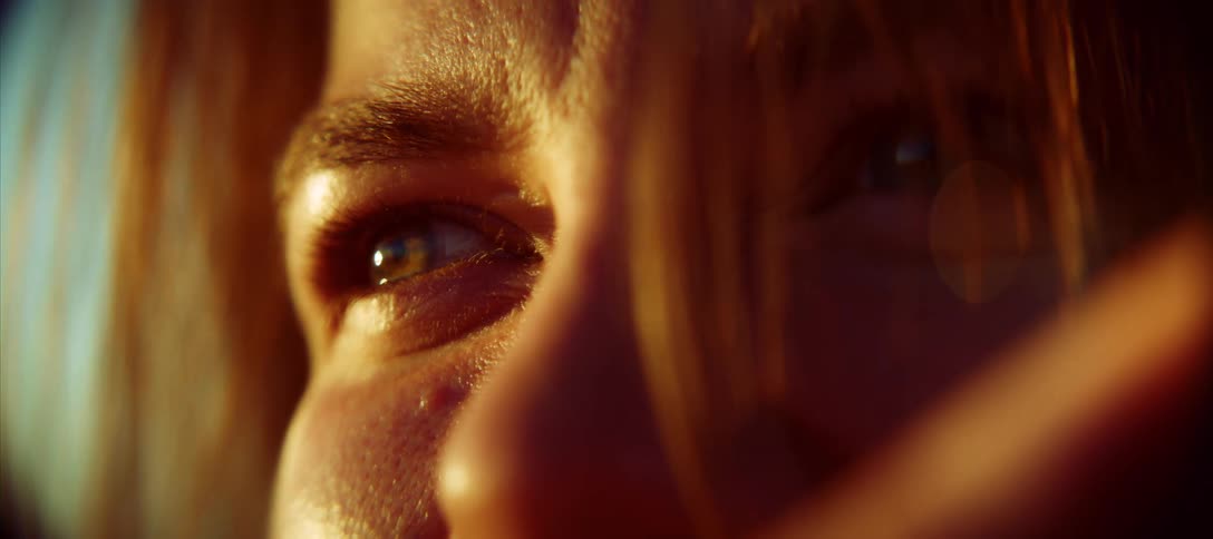 A tight shot shows a persons eyes nose and cheek illuminated by the golden light of the setting sun their eyes are a striking bluegreen and they are looking up and to the left