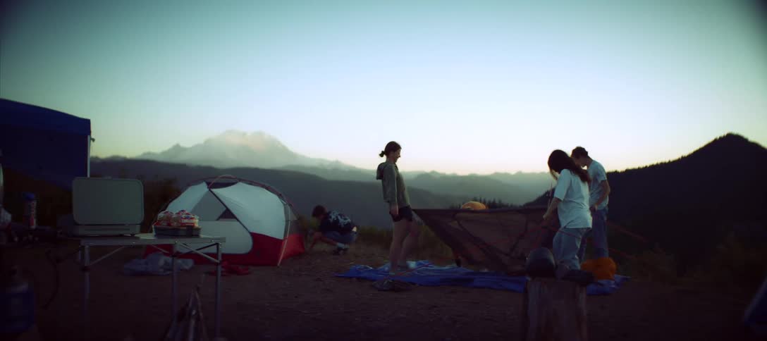 On a mountain plateau having already put together a sleeping tent a group of friends struggles to put together another tent