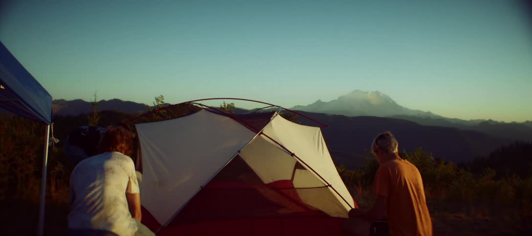 Three people are setting up a tent on a mountain ridge at sunset