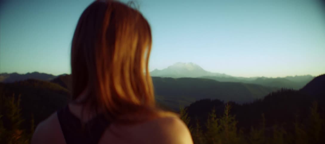 A woman is standing and looking at a landscape with mountains in the background