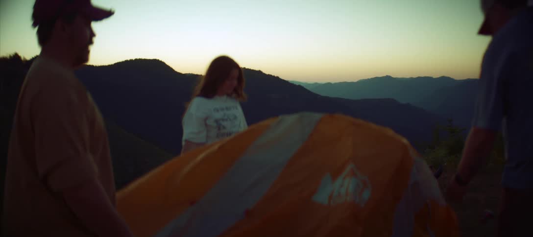 A group of people sets up a tent in the mountains at sunset