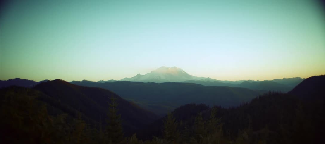A man at a campsite looks out at a majestic snowcapped mountain range during a serene sunrise before the shot settles on the scenic landscape view