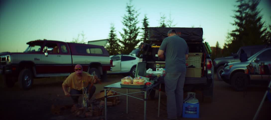 Men take part in a wilderness outing by building a campfire and cooking on a grill