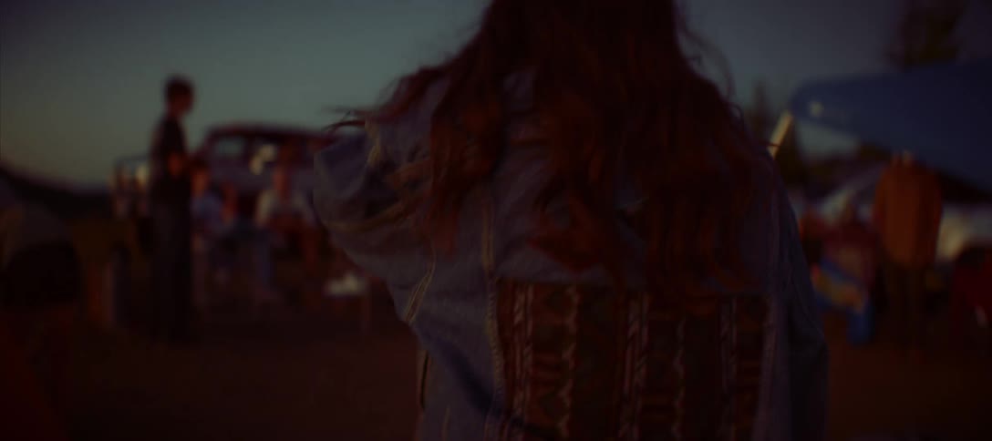 A woman with long hair walks toward a campsite at dusk