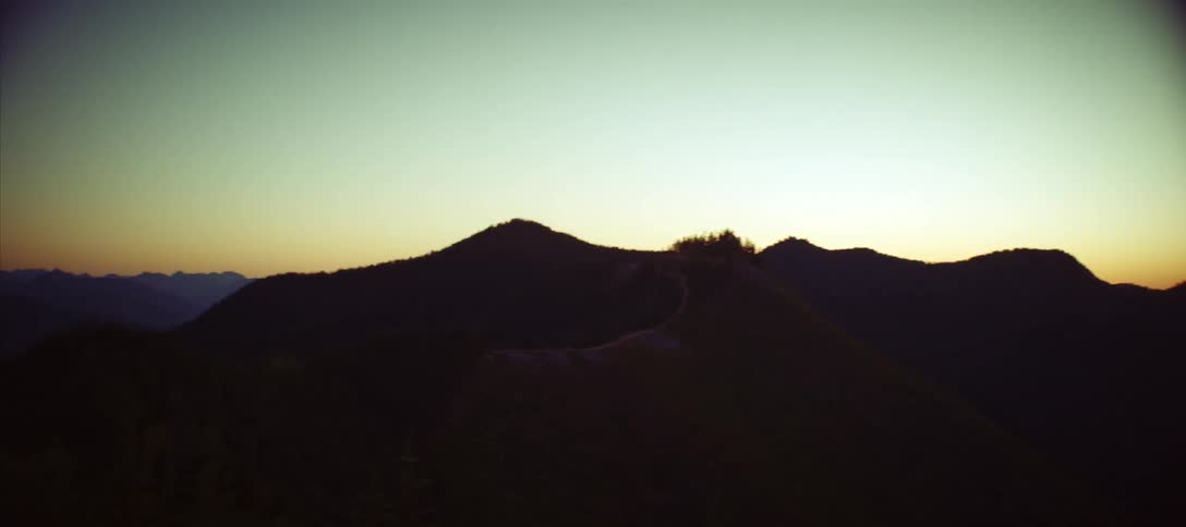 A view of a mountain range at dawn with the sun rising behind the mountains and the camera panning across the landscape