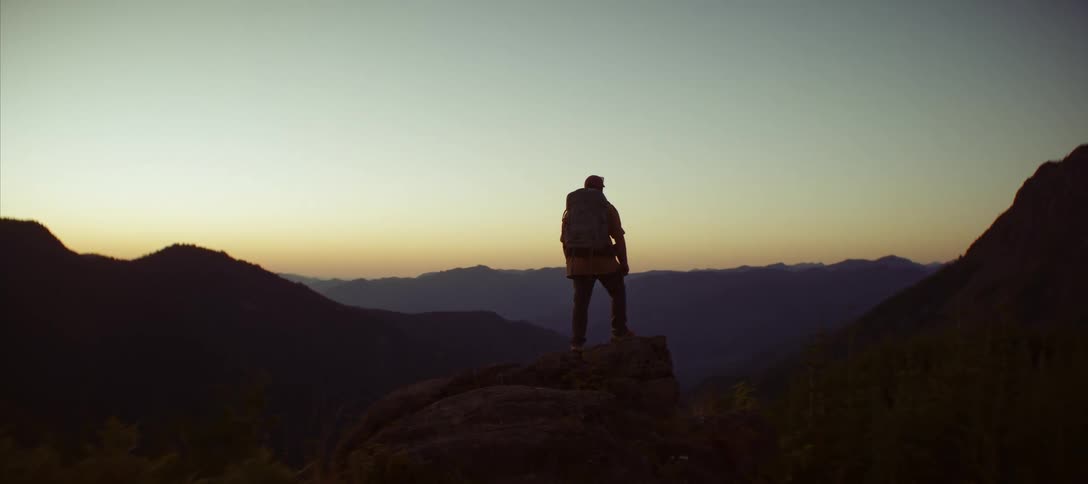 Man with hiking backpack on a mountain peak overlooking a landscape in the late afternoon