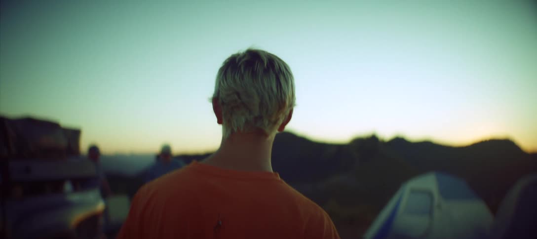 A person walks toward camping tents in the mountains at sunset