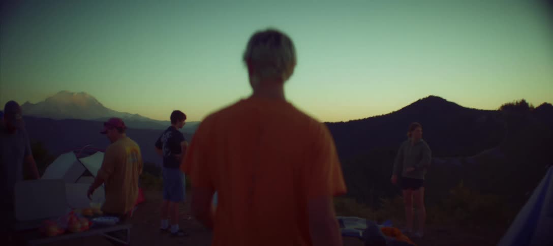 A person walks toward camping tents in the mountains at sunset