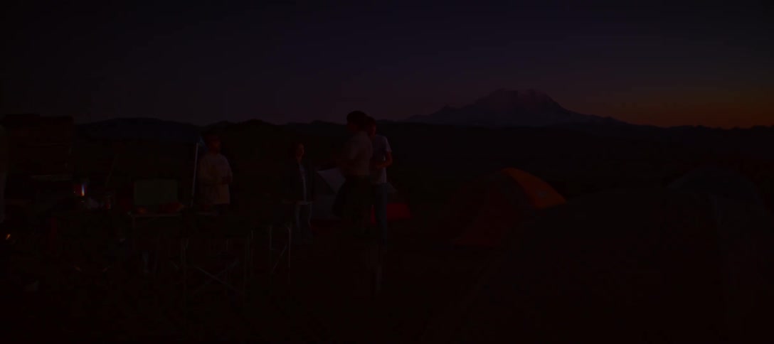 Five people are standing at a campsite with a tent and a mountain in the background at a nighttime setting